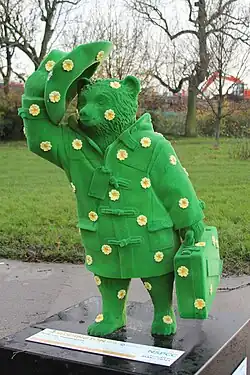 Una estatua del Oso Paddington completamente verde con múltiples flores pegadas como adorno