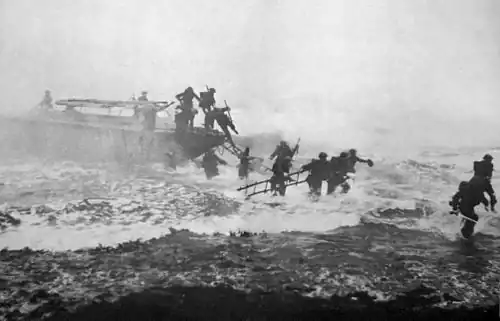 Fotografía en blanco y negro de soldados uniformados saliendo de un bote Eureka en aguas agitadas llevando escalas, con Churchill al mando a la derecha, con su espada visible en la mano derecha