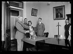 John J. Pershing sosteniendo a su perro el sargento. Stubby, mientras Robert Conroy, vestido de traje, se para detrás de ellos.