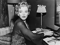 Monroe, con una bata de encaje transparente y aretes de diamantes, sentada en un tocador y mirando fuera de cámara con una expresión de asombro.